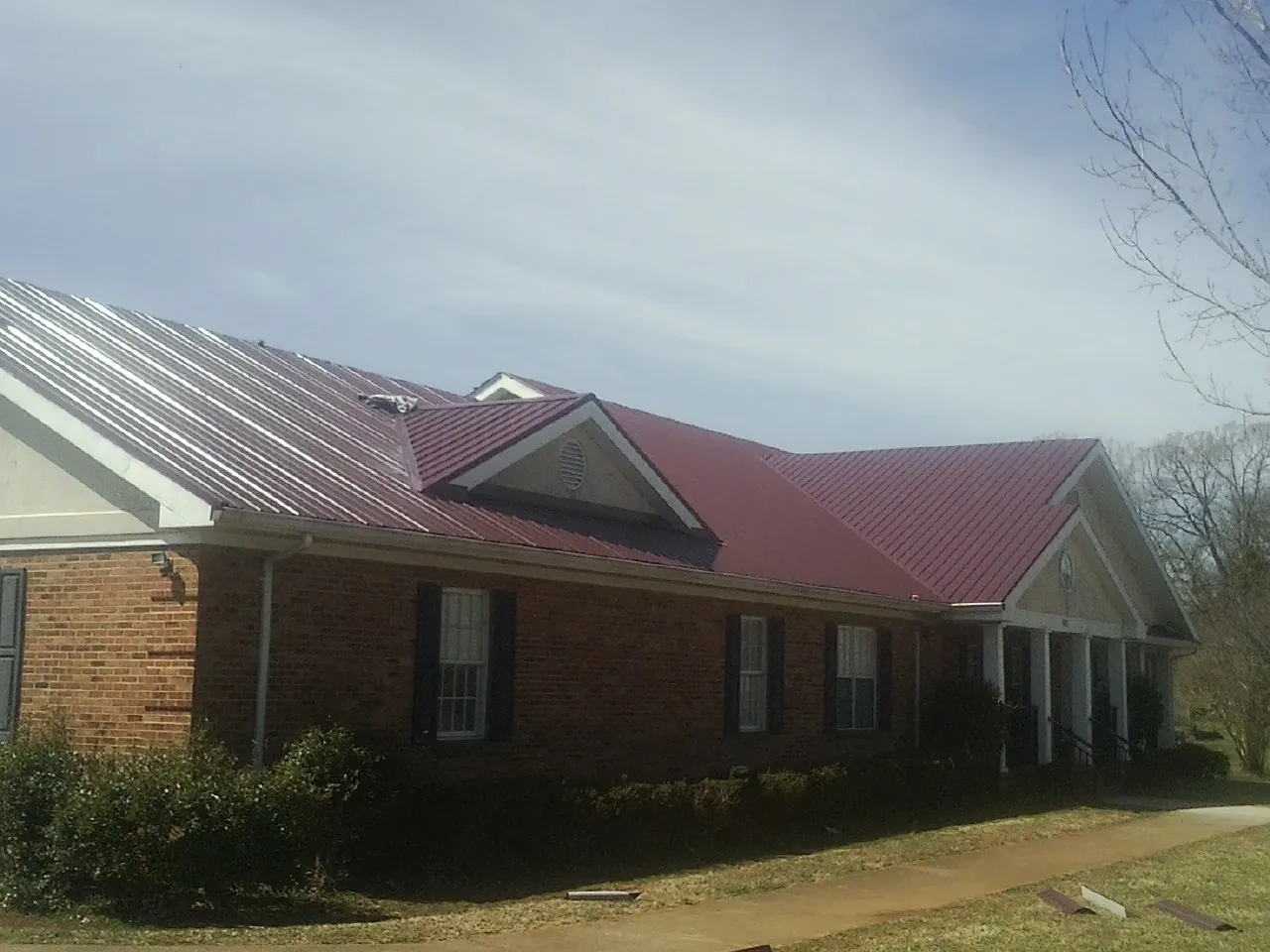 Red metal roof with gabled entries on a long brick building, from a Hail Damage Roof Repair job in Maricopa