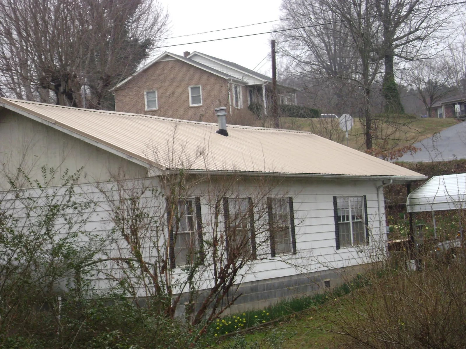 Tan metal roof on a white sided house set into a hillside — Commercial Roofing by Roofing Brothers in Maricopa